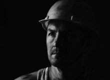 Dirty coal miner in a yellow hard hat on a dark background in a black and white photo